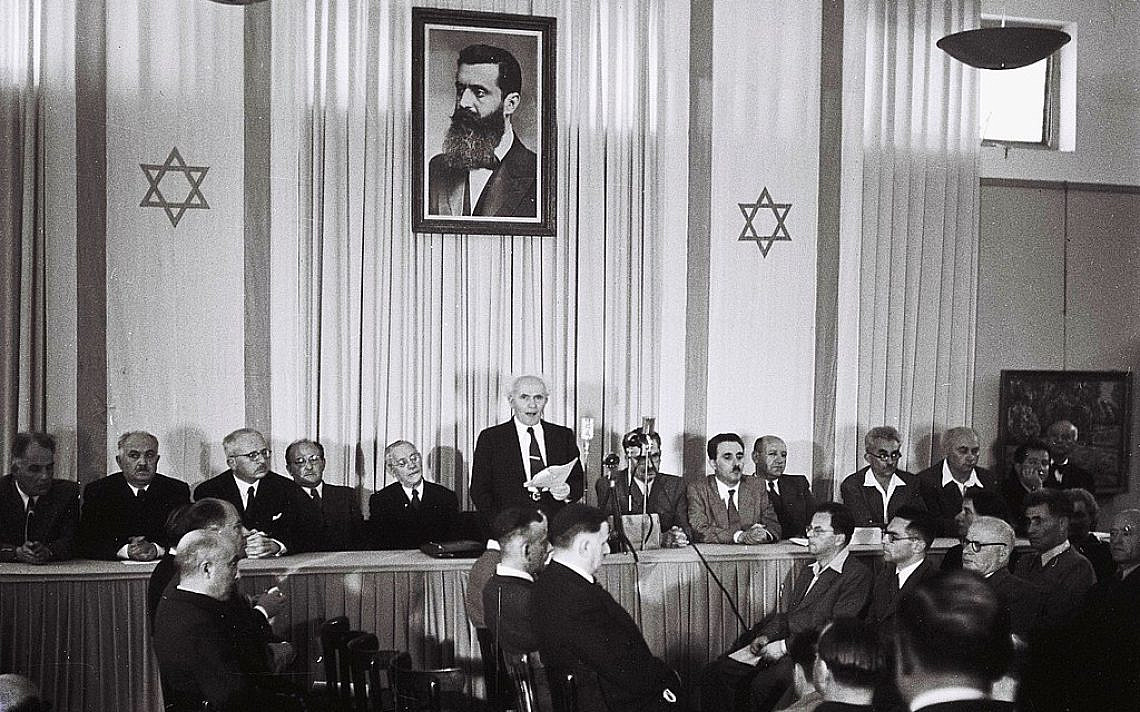 בן גוריון מכריז על הקמת מדינ תנת ישראל כשברקע תמונת הרצת ושני דגלי המדינה בצדדים. צילום: ויקיפדיה